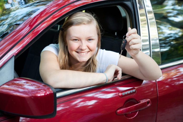 teenage girl sitting in her new car while holding the car keys