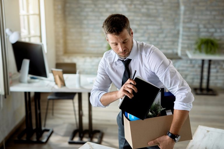 professionally dressed man carrying a cardboard box with his belongings in it