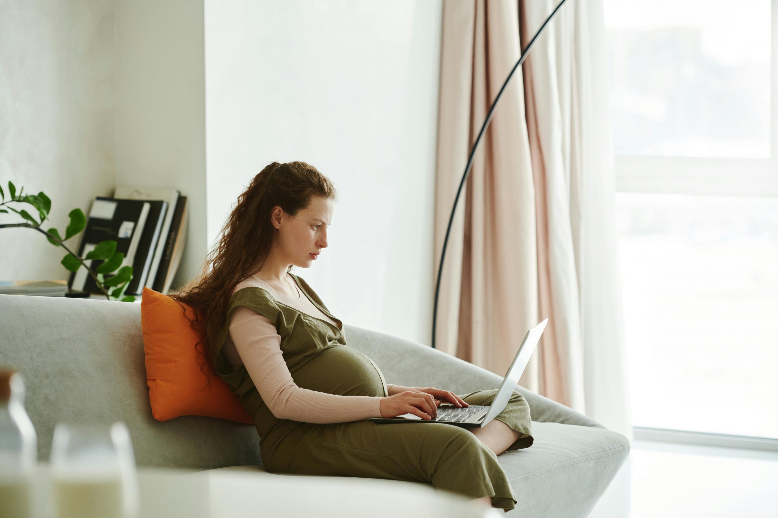 pregnant woman sitting on a couch, using a laptop